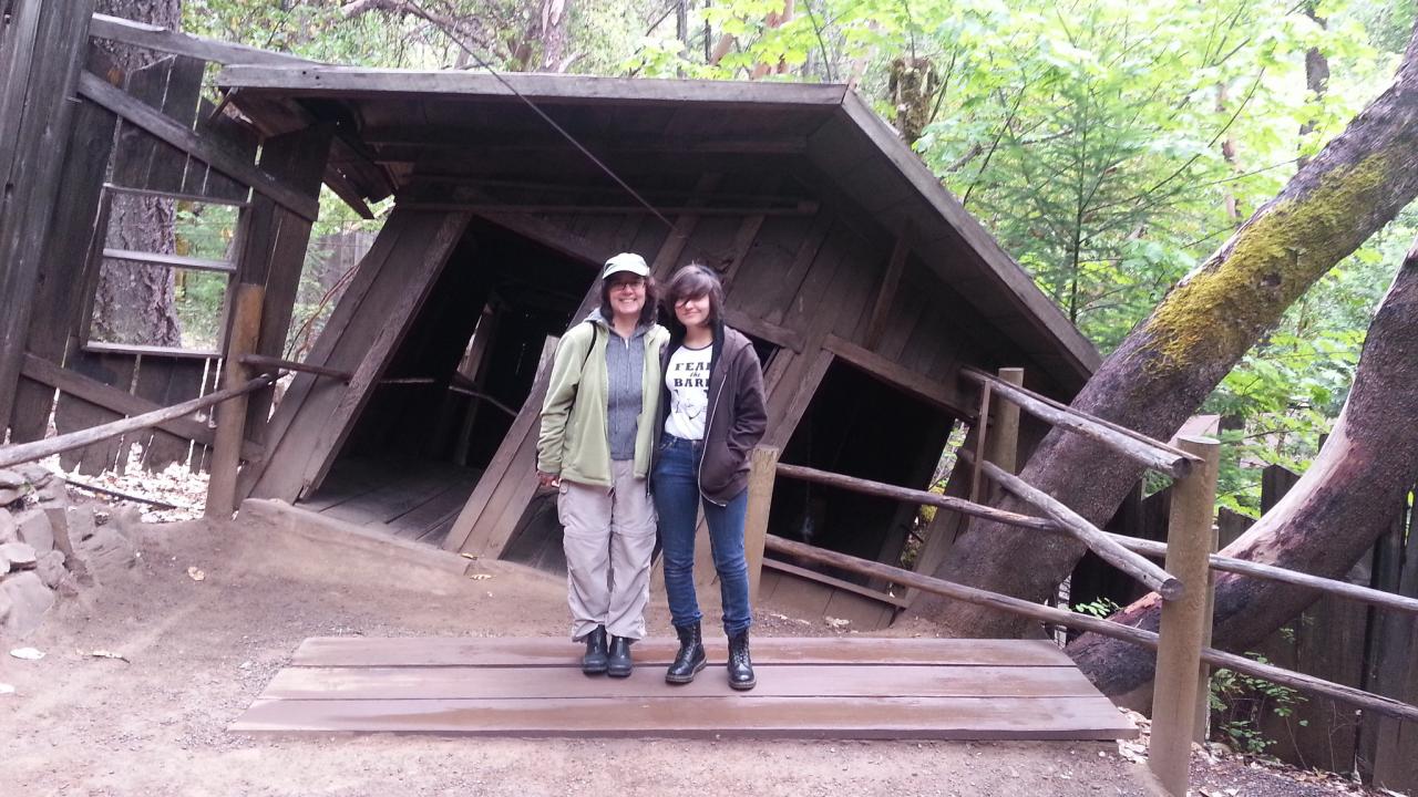 Two people standing in front of a crooked house in the woods
