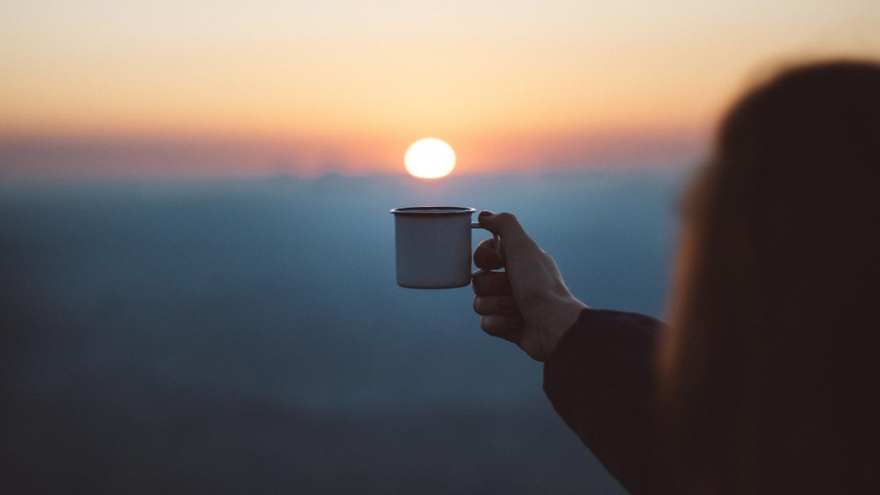 someone holding a mug under the setting sun in the background