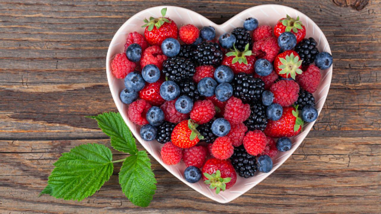 A Heart bowl on a wooden table filled with berries 