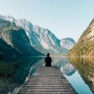person sitting on a dock looking out to a lake surrounded by mountains